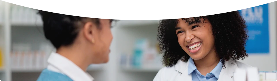 A pharmacist smiling while speaking with a colleague.