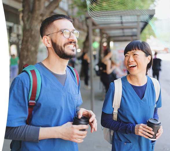 Two healthcare professionals in scrubs smiling while walking outdoors with coffee