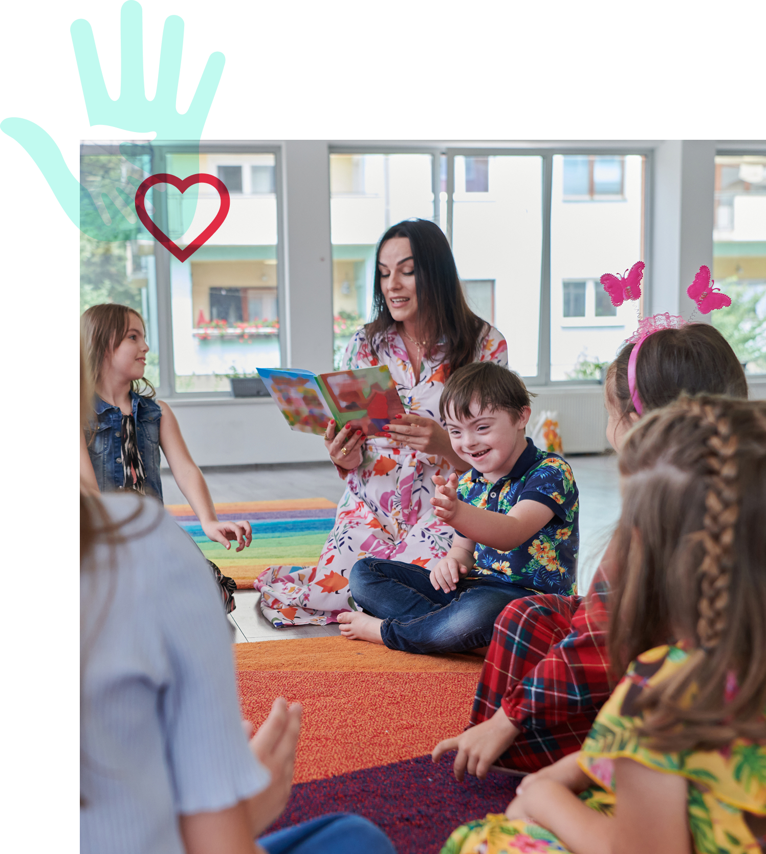 A teacher reads a book to a group of young children sitting on a colorful rug, with one boy smiling brightly. A translucent teal hand with a red heart is overlaid above.