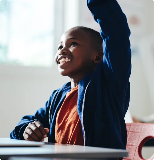 A young student raising their hand in a classroom.